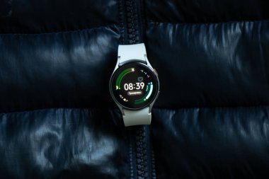 Ukrayna Dnepr 08.01.2021 - Akıllı saatler Samsung Galaxy Galaxy 4 pisti gri kayışlı yumuşak, şişirilmiş bir kış siyah ceketi, teknoloji