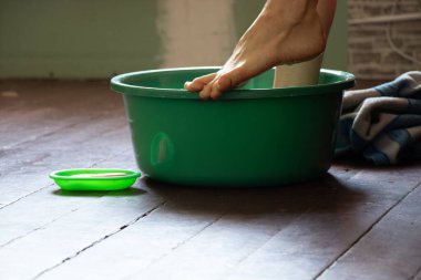 Bir kız ayaklarını evdeki ahşap zeminde suyla yeşil bir havuzda yıkıyor, ayak bakımını yapıyor, ayaklarını evde yıkıyor, temizlik yapıyor, havuzda yüzüyor.