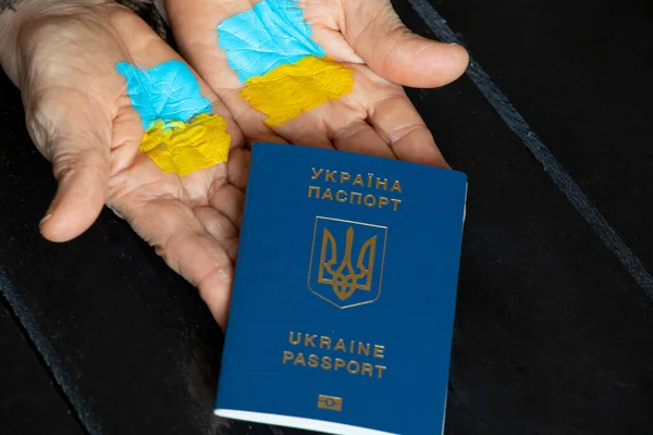 The national flag of Ukraine is drawn on the hands of a woman and next to a foreign passport on the table, stop war and peace, the flag of Ukraine