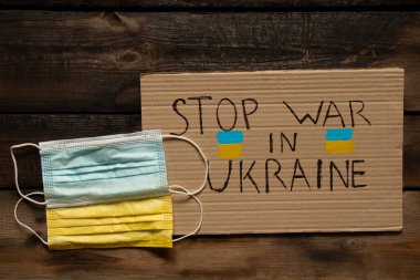 Tıbbi maskeler, Ukrayna bayrağı gibi sarı ve mavi, ahşap bir masada yatıyor ve yazılı bir işaret Ukrayna 'daki savaşı durduruyor. Ukrayna bayrağı, Rusya saldırganı. Ukrayna 2022 'deki savaş sırasında tıp.