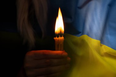 The girl is holding a candle and praying for Ukraine against the background of the flag of Ukraine, we all grieve and pray for peace, vryna in Ukraine, a hand with a candle, prayer clipart