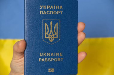 Bir el, Ukrayna 'nın sarı-mavi bayrağının arkasında, barışçıl ülkemiz Ukrayna' nın yabancı pasaportunu tutuyor.