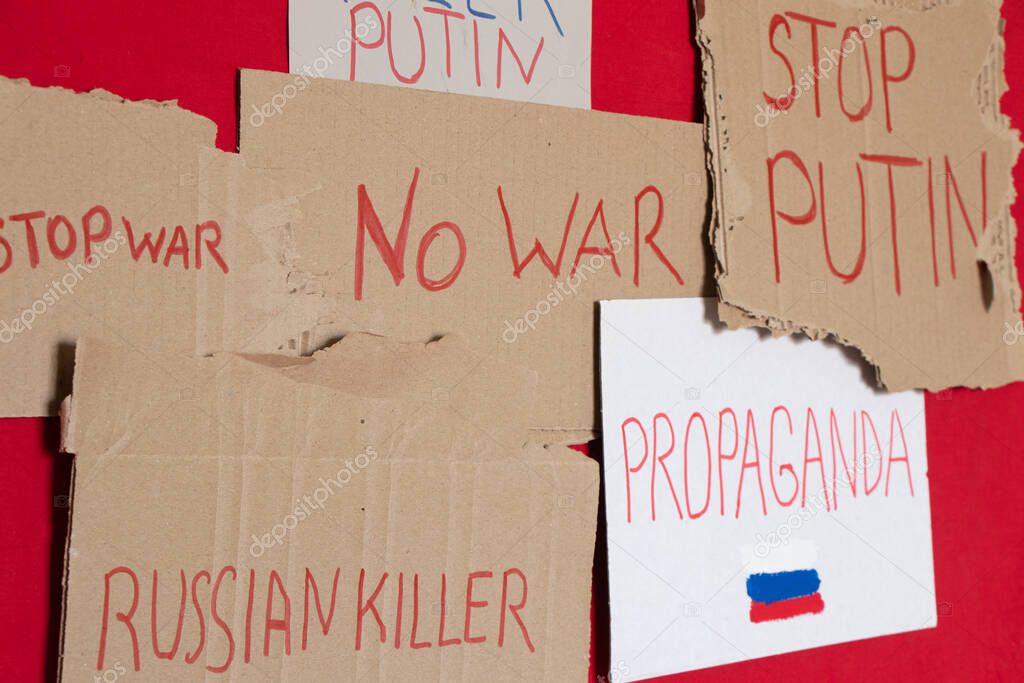 Paper signs with slogans stop war, Russian killer, propaganda, killer Putin, stop Putin, no war on a red background, protest action 2022