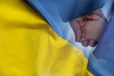 Anne, Ukrayna 'nın sarı-mavi bayrağının arka planında küçük bir kızın elini tutuyor. Ukrayna 'da barış, 2022 savaşını durdurun.