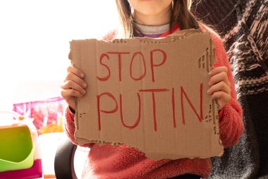 Küçük bir kız elinde Putin 'i Ukrayna' daki evinde durdurup Ukrayna 'daki savaşı durdurmak isteyen bir poster tutuyor.
