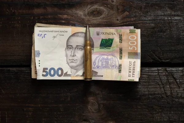 一颗子弹和乌克兰格里夫尼亚的钱躺在一张木制桌子上 钱被用来购买士兵的军用武器 2022年的乌克兰战争 — 图库照片