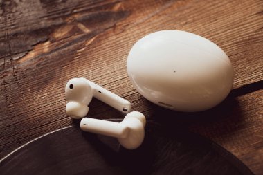 Kablosuz kulaklıklar ve şarj çantası plak, müzik ve hobilerin olduğu ahşap bir masanın üzerinde duruyor.