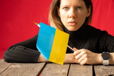 Bir kız evinde bir masada oturuyor ve Ukrayna 'nın ulusal bayrağını kırmızı bir duvarın arkasında tutuyor, Ukrayna' daki savaşı durduruyor, Ben Ukraynalıyım 2022