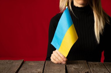 Bir kız evinde bir masada oturuyor ve Ukrayna 'nın ulusal bayrağını kırmızı bir duvarın arkasında tutuyor, Ukrayna' daki savaşı durduruyor, Ben Ukraynalıyım 2022