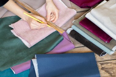 Kadın elleri masadaki farklı kumaş parçalarını kesiyor, terzi atölyesi, dikiş ve moda, terzilik.