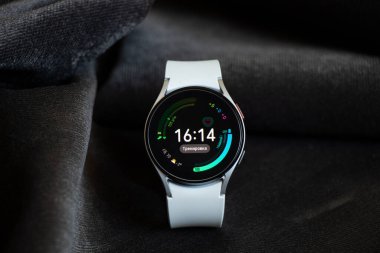 Ukrayna Dnepr 19.03.2022 - Akıllı saat Samsung Galaxy 4.40 mm kadınlar için beyaz bir kayış üzerinde masanın üzerinde kırışık kumaş, teknolojiler