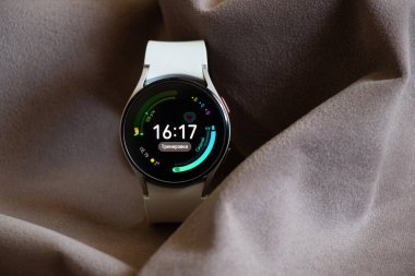 Ukrayna Dnepr 19.03.2022 - Akıllı saat Samsung Galaxy 4.40 mm kadınlar için beyaz bir kayış üzerinde masanın üzerinde kırışık kumaş, teknolojiler