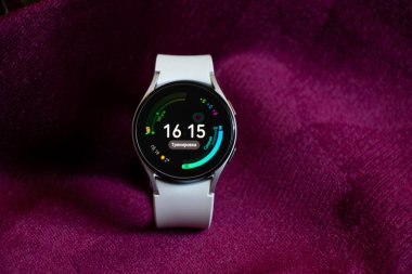 Ukrayna Dnepr 19.03.2022 - Akıllı saat Samsung Galaxy 4.40 mm kadınlar için beyaz bir kayış üzerinde masanın üzerinde kırışık kumaş, teknolojiler