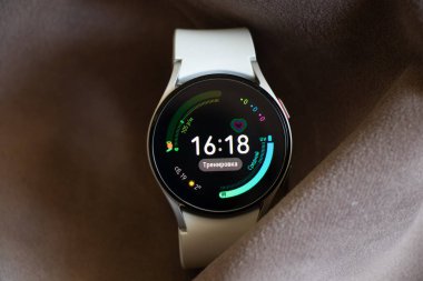 Ukrayna Dnepr 19.03.2022 - Akıllı saat Samsung Galaxy 4.40 mm kadınlar için beyaz bir kayış üzerinde masanın üzerinde kırışık kumaş, teknolojiler