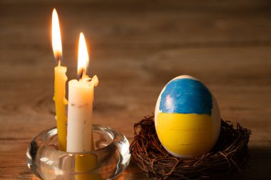 Bir beyaz tavuk yumurtası, Ukrayna 'nın boyalı bayrağıyla evdeki bir masada mum alevi, kültür ve bayramlar 2022