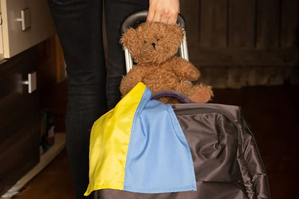Ukraynalı bavullu bir kadın ve Ukrayna bayrağı taşıyan bir oyuncak ayı savaş yüzünden evinden ayrılıyor, Ukraynalı mülteciler, 2022 'de evlerini terk ediyor.