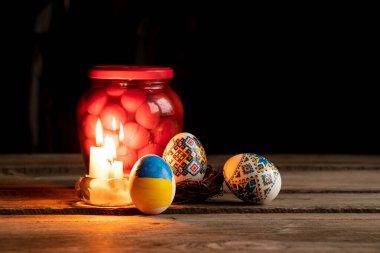 Ukrayna 'da, Ukrayna' nın karanlık ve Paskalya bayramında 2022 savaşında boyalı bir Ukrayna bayrağı, bir kavanoz domates ve bir mum alevi ile evlerin masasına boyanmış tavuk yumurtaları.