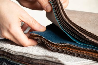 Bir kızın elindeki kumaşların farklı renklerinden oluşan bir katalog döşeme için bir müşteri seçimi, arka plan olarak çok renkli kumaş örnekleri, modaya uygun kumaşlar