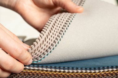 Bir kızın elindeki kumaşların farklı renklerinden oluşan bir katalog döşeme için bir müşteri seçimi, arka plan olarak çok renkli kumaş örnekleri, modaya uygun kumaşlar