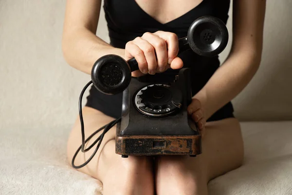 Viejo teléfono retro negro en las piernas de una mujer de cerca, una llamada al teléfono — Foto de Stock
