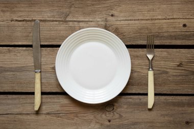 Bir beyaz tabak ve bıçaklı bir çatal evdeki mutfaktaki eski ahşap bir masanın üzerinde duruyor. Restoran işi, mutfak aletleri.