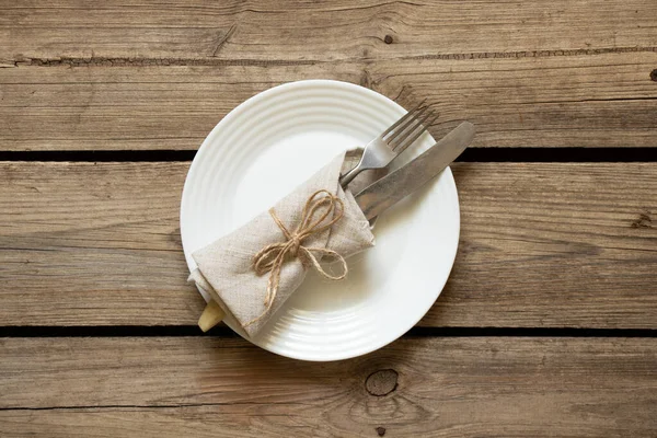 Bir beyaz tabak ve bıçaklı bir çatal evdeki mutfaktaki eski ahşap bir masanın üzerinde duruyor. Restoran işi, mutfak aletleri.