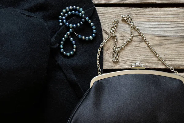 Siyah kadın şapkası ve siyah bir akşam çantası ve ahşap bir masa üzerinde inci boncuklar, moda ve trend, güzellik ve aksesuarlar