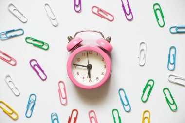 Çok renkli ataçların etrafında pembe bir çalar saat beyaz bir arkaplanda duruyor, zaman, kırık