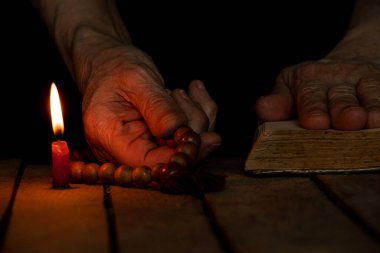 A woman with a wooden rosary and a bible vomited candles in the dark, a woman prays, praying, faith and religion,temple