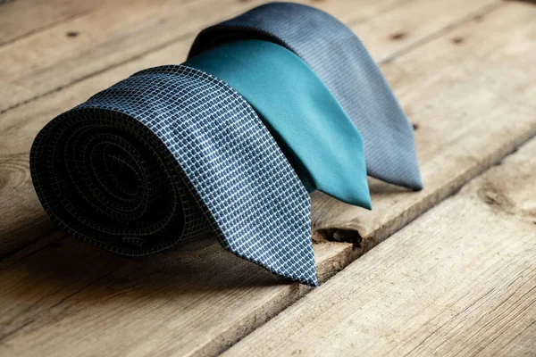Üç mavi kravat ahşap bir masada yatıyor, farklı adamların bağları yakın plan.