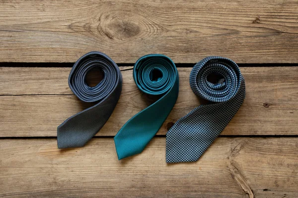 Üç mavi kravat ahşap bir masada yatıyor, farklı adamların bağları yakın plan.