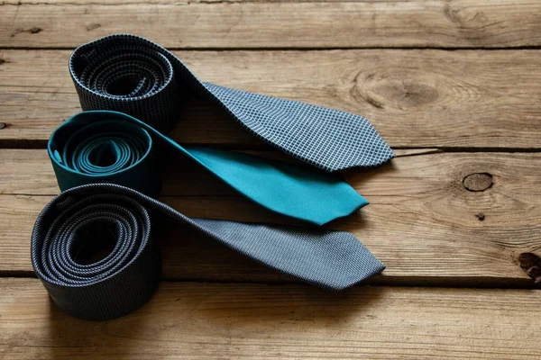 Üç mavi kravat ahşap bir masada yatıyor, farklı adamların bağları yakın plan.