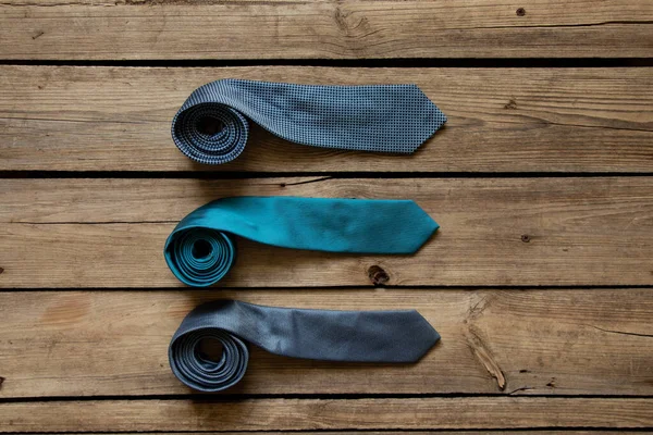 Üç mavi kravat ahşap bir masada yatıyor, farklı adamların bağları yakın plan.