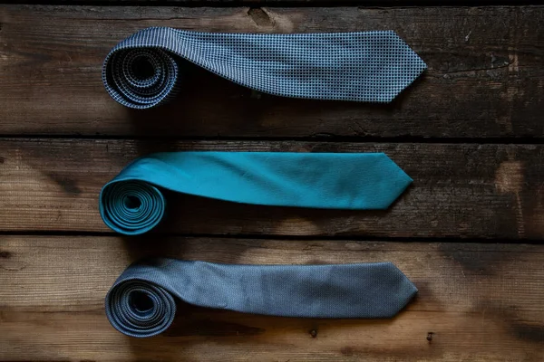 Üç mavi kravat ahşap bir masada yatıyor, farklı adamların bağları yakın plan.
