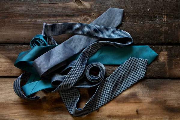 Üç mavi kravat ahşap bir masada yatıyor, farklı adamların bağları yakın plan.