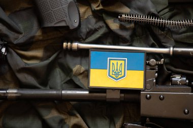 Ukrayna bayrağı, sökülmüş bir makineli tüfekte yeşil kamuflaj kumaşında, Ukrayna 'daki savaşta, askeri silahlarda yatıyor.