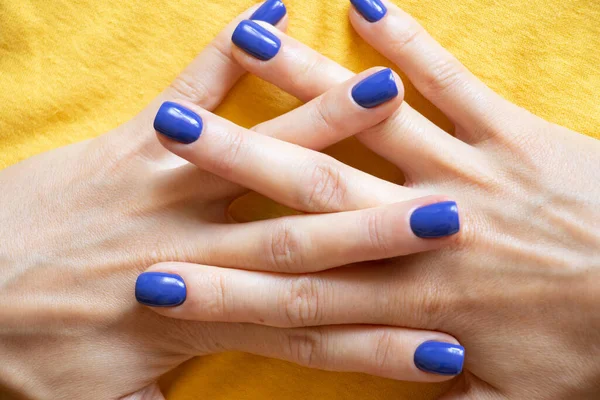 Manicure and blue polish on the girl\'s finger on a yellow background, yellow-blue color of the flag of Ukraine, gel polish on the girl\'s nails, manicure