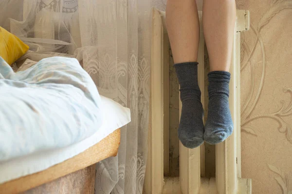 Women's feet in socks on an old cast-iron battery in an apartment in winter, a cold apartment, a heating season, a battery in an apartment, it's cold