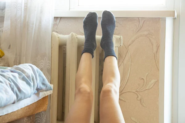 Women\'s feet in socks on an old cast-iron battery in an apartment in winter, a cold apartment, a heating season, a battery in an apartment, it\'s cold