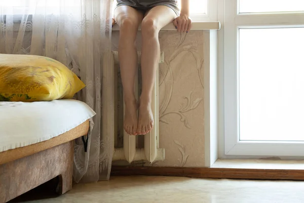 Womens feet on an old cast-iron battery in an apartment in winter, a cold apartment, a heating season, a battery in an apartment, its cold