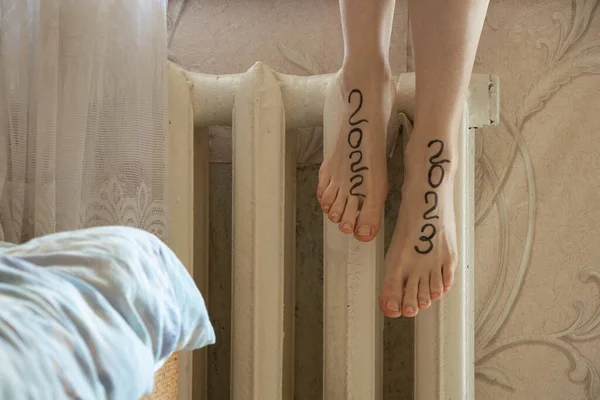 2023 and 2022 are written on the legs of a girl who sits on an old heating battery in the apartment, the beginning of a new year, happy new year 2023