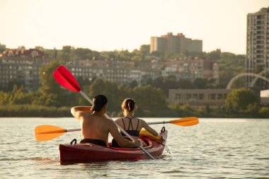 Bir kız ve bir adam, Ukrayna 2022 'deki savaş sırasında kano ve şehir manzarasıyla şehir boyunca Dinyeper Nehri boyunca yelken açıyorlar.