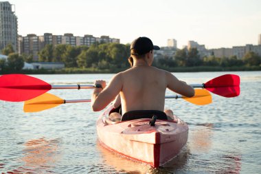 Bir kız ve bir adam, Ukrayna 2022 'deki savaş sırasında kano ve şehir manzarasıyla şehir boyunca Dinyeper Nehri boyunca yelken açıyorlar.