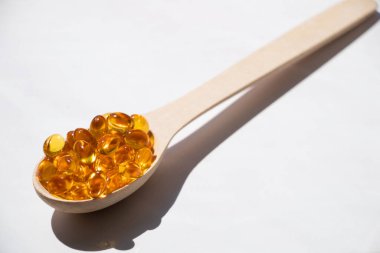 Fish oil pills lie in a wooden spoon on an isolated background, vitamins and supplements, health