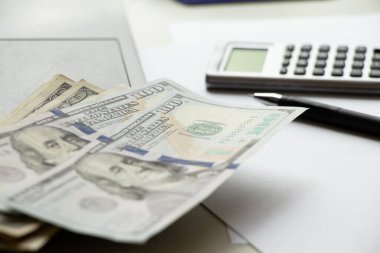 One hundred dollars lie on a laptop on the table and next to it lies a calculator and a pen, business and finance, economics
