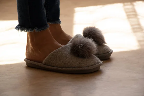 A girl in gray soft slippers with a bubo on the floor at home, home shoes, room slippers and feet