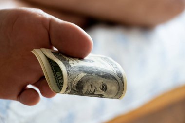 Man's foot holding one hundred dollars with toes lying on the bed at home, passive income, business and work, leisure and money, money in feet