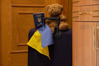 A suitcase with a teddy bear flag of Ukraine and a biometric foreign passport of Ukraine stands in the corridor at the exit from the house, Ukrainian refugees