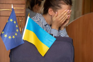 A girl is crying near a suitcase with flags of Ukraine and the flag of the European Union at home before leaving Ukraine because of the war