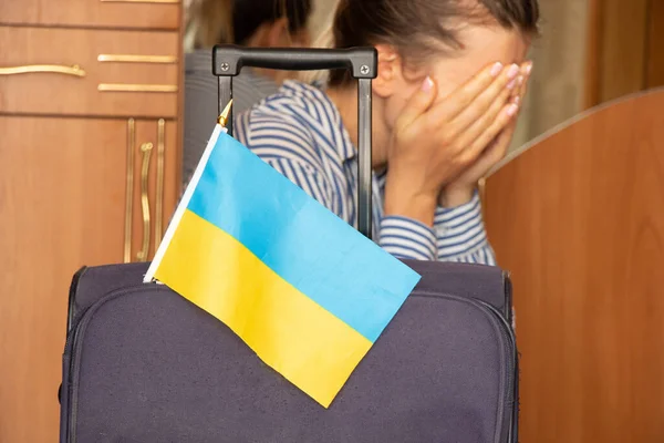 A girl cries near a suitcase with Ukrainian flags at home before leaving her home in Ukraine because of the war